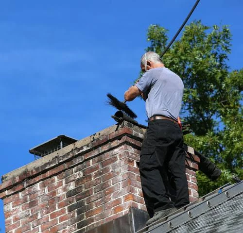 Worker brushing a brick chimney above a shingled roof