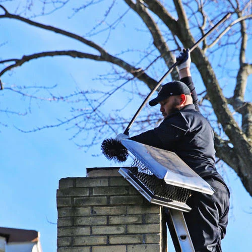 Technician holding a metal chimney cap beside a brick chimney
