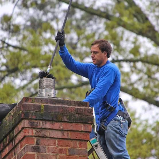 Chimney sweep in a blue shirt cleaning a rooftop flue with a brush