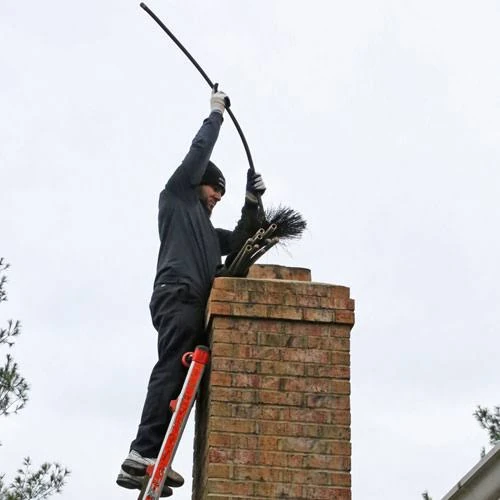 Chimney sweep working a long brush into a residential brick chimney