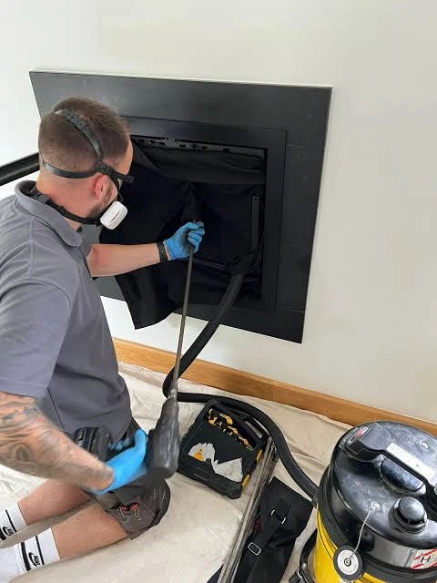 Technician wearing a respirator while cleaning inside a fireplace insert