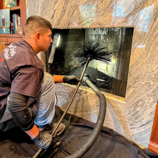 Technician cleaning a stone-surround fireplace with a chimney brush and vacuum