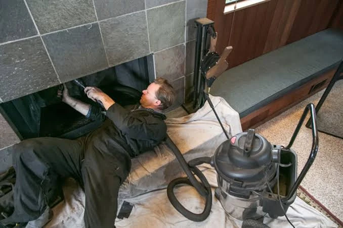 Technician cleaning a tiled fireplace with vacuum equipment and protective floor coverings