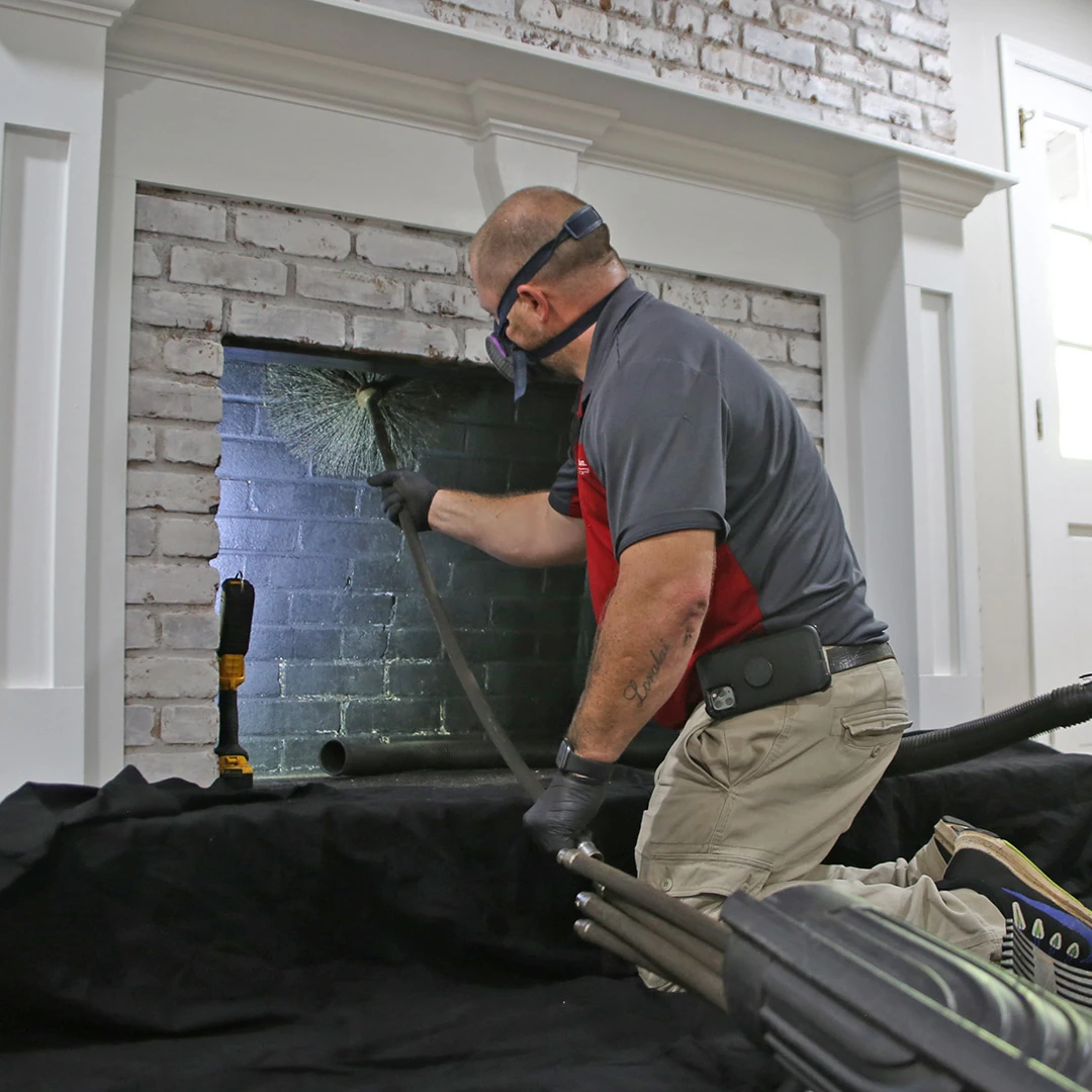 Chimney technician using a rotary brush inside a white brick fireplace